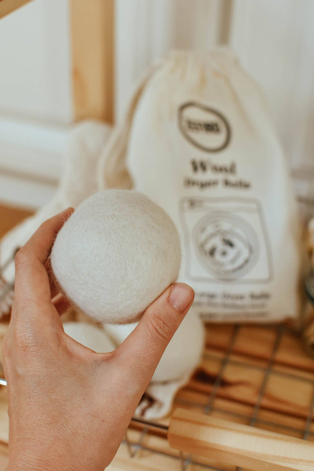 Hand holding a white dryer ball with a branded bag in the background on a wooden surface.