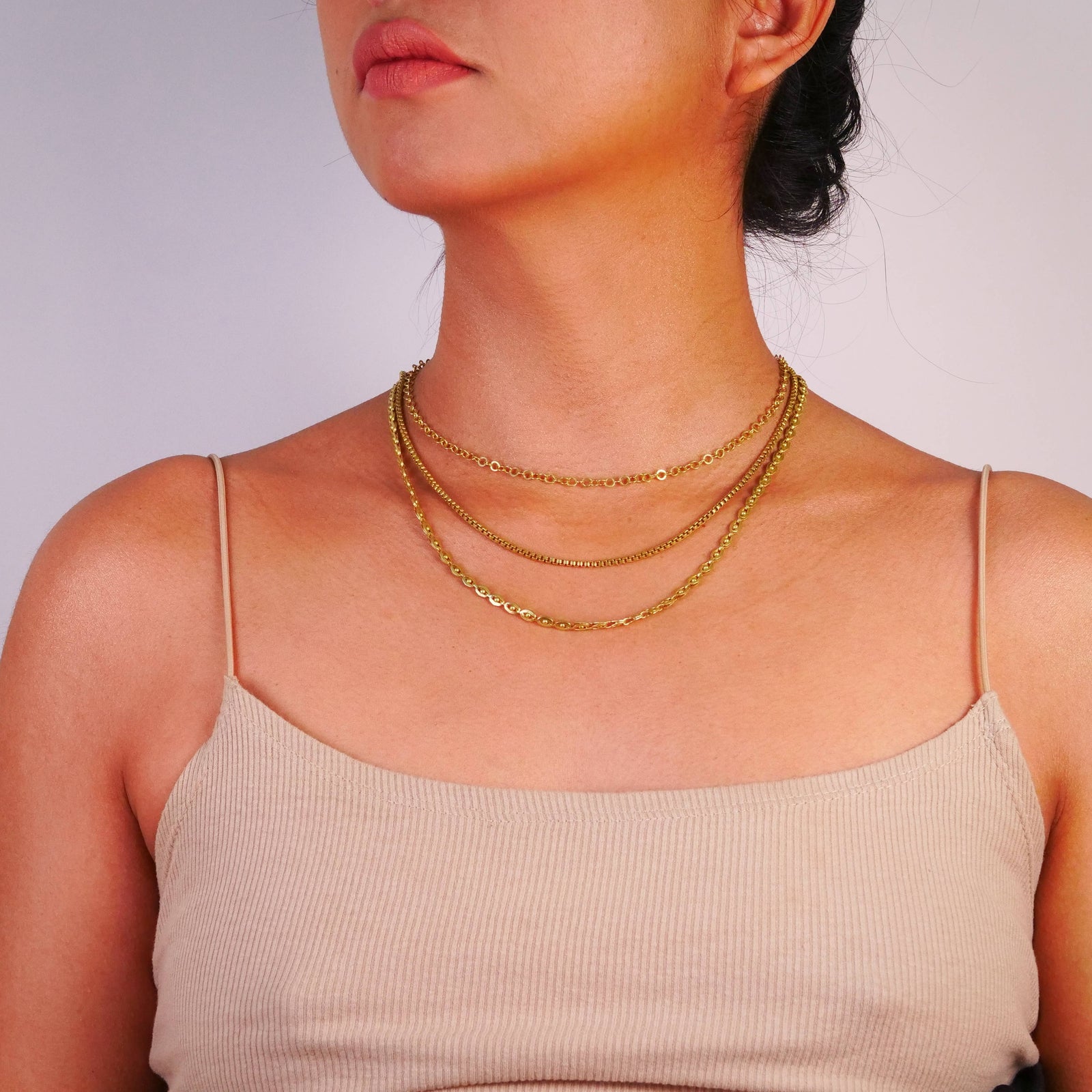 Woman wearing three brass necklace with a plain background