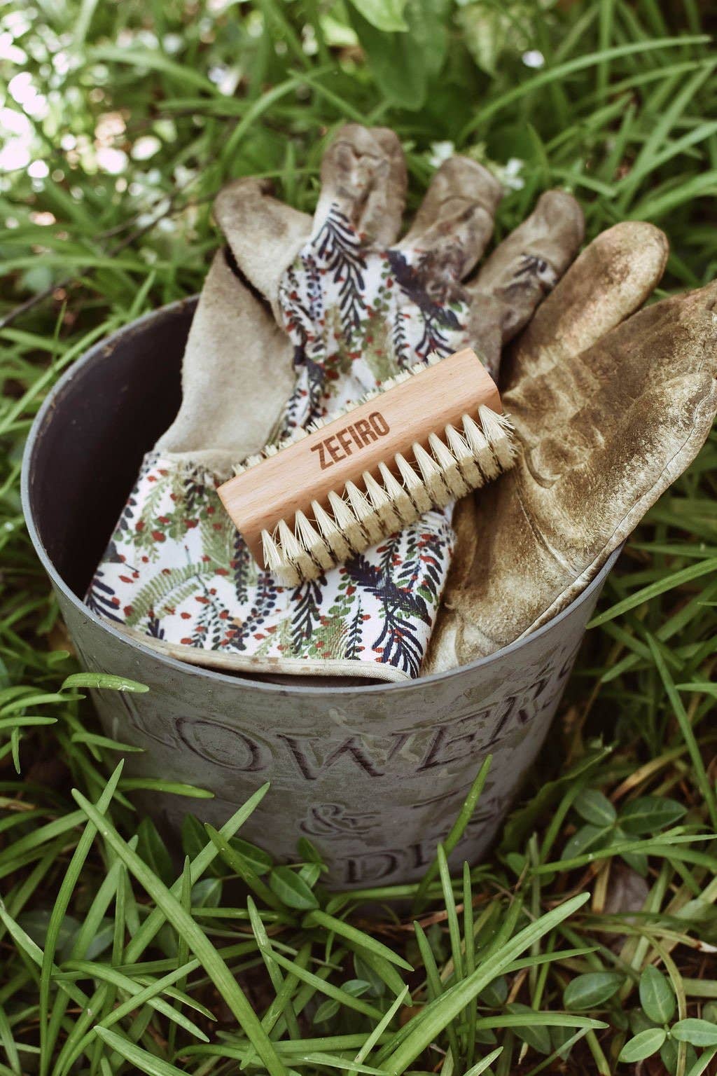 Gardening tools including gloves and a nail brush in a metal container on grass