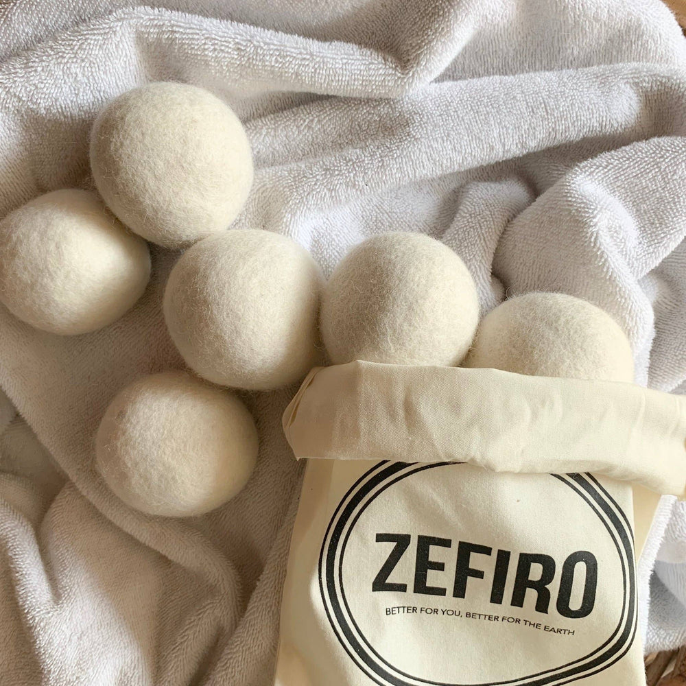 White wool dryer balls on a white cloth with a Zefiro bag.