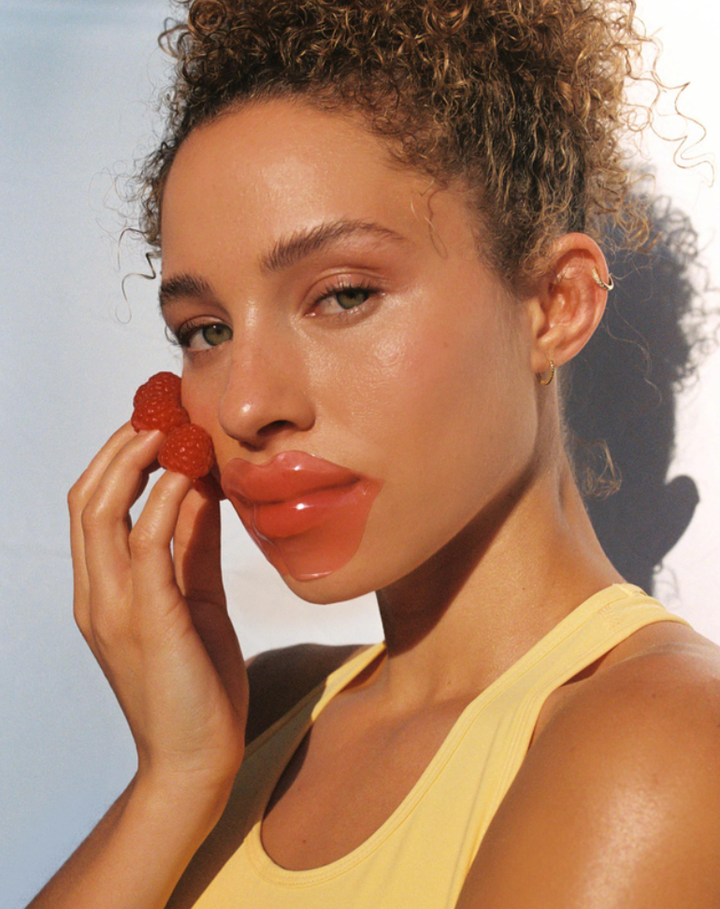 model wearing lip patch with hands to face, raspberries on finger tips
