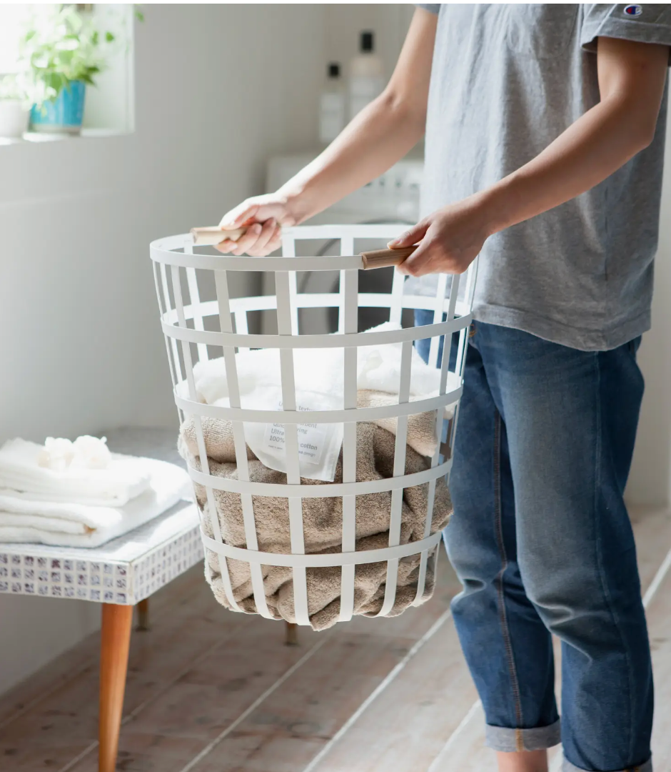 man in a laundry room holding a white laundry basket, wooden handle